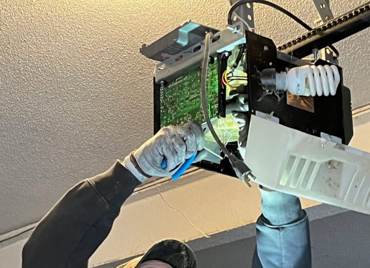 a professional technician repairing a garage door opener, showcasing various tools and equipment used during the repair process. The technician is wearing a uniform with a logo representing Garage Door Repair Services Cloud FL, emphasizing expertise and quality service. The background shows a neatly organized workshop with various garage door components. This image highlights the reliable and efficient garage door opener repair services offered by the company.